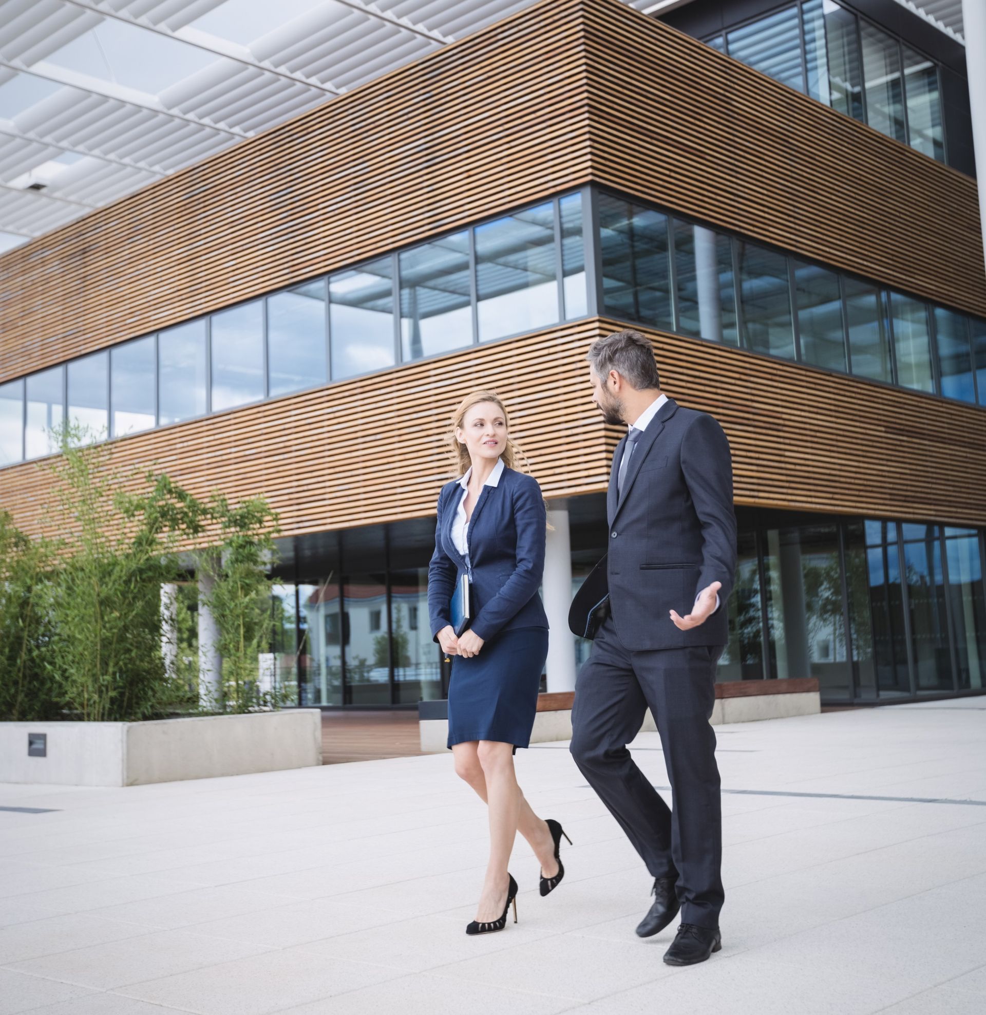 Two business people walking outside a modern office building with glass and wood panels