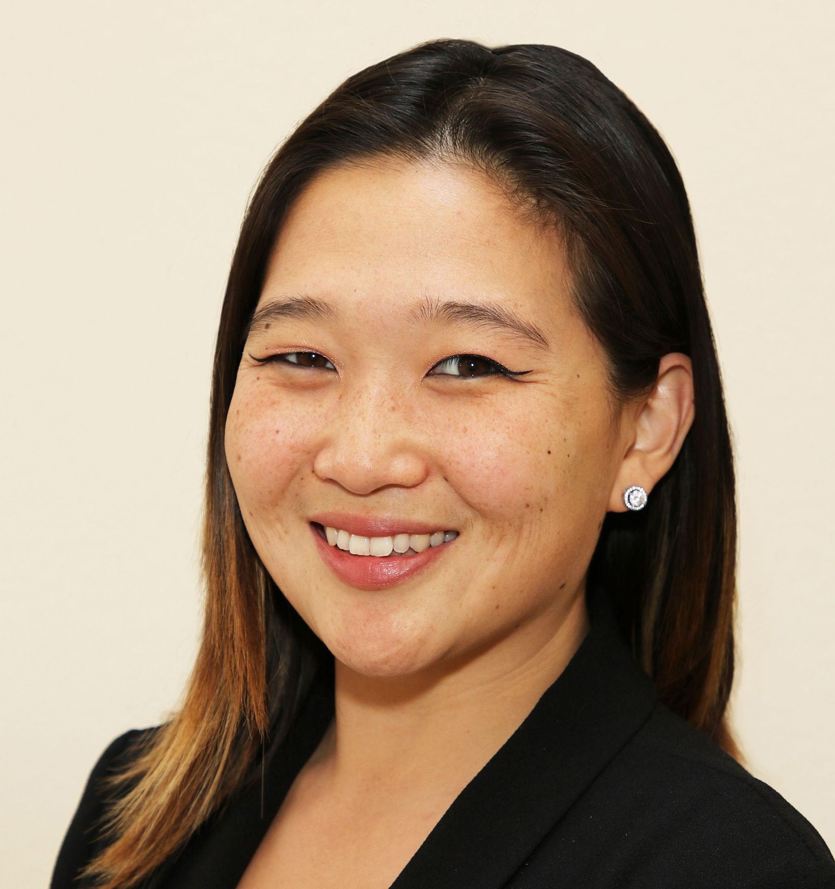 A woman with long dark hair is smiling and wearing a black jacket.