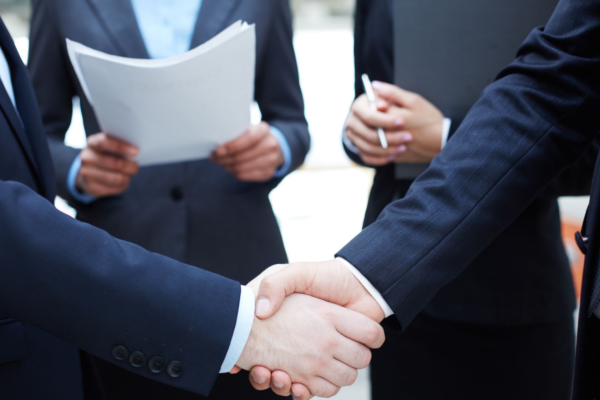 Two men in suits are shaking hands on a balcony.