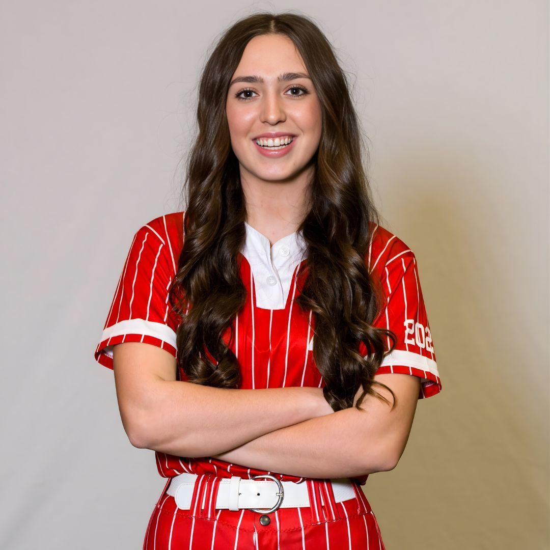 Smiling person in a red and white pinstriped athletic uniform with arms crossed, set against a plain light background.