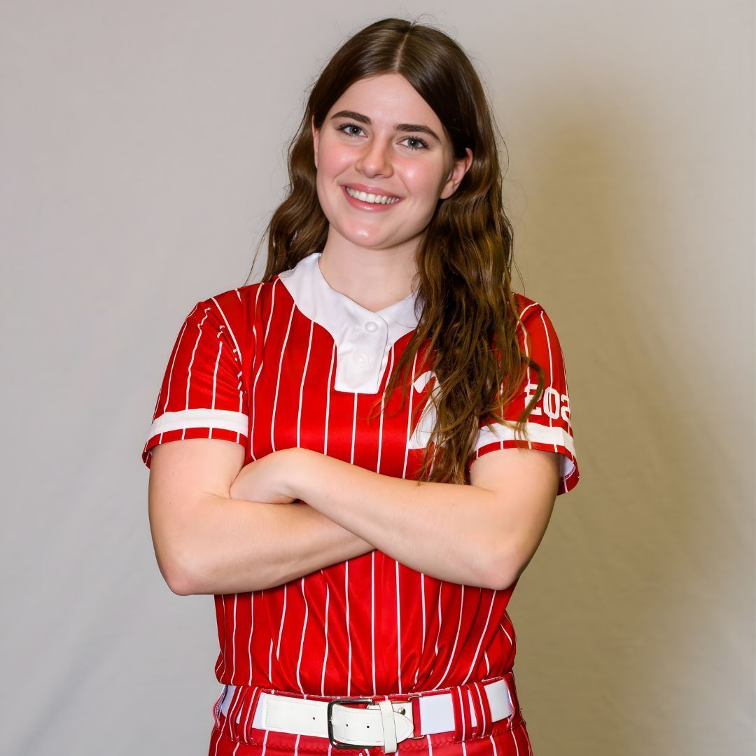 A person wearing a red and white pinstriped sports jersey with crossed arms, smiling against a plain grey background.