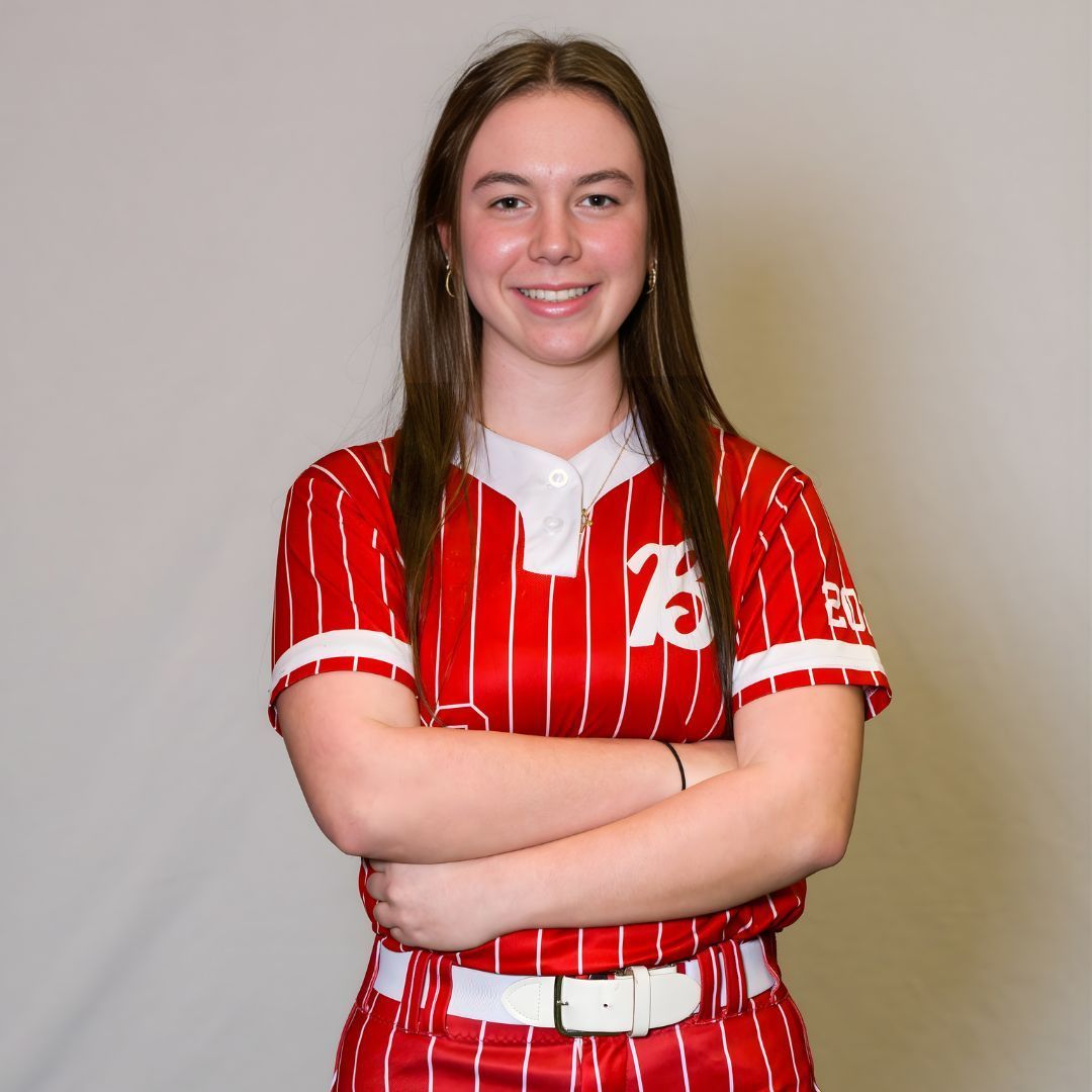 A person in a red and white pinstriped baseball uniform with arms crossed, smiling against a neutral background.