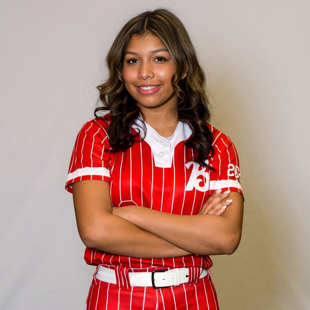 A smiling athlete stands against a plain background, wearing a red pinstriped uniform with arms crossed.