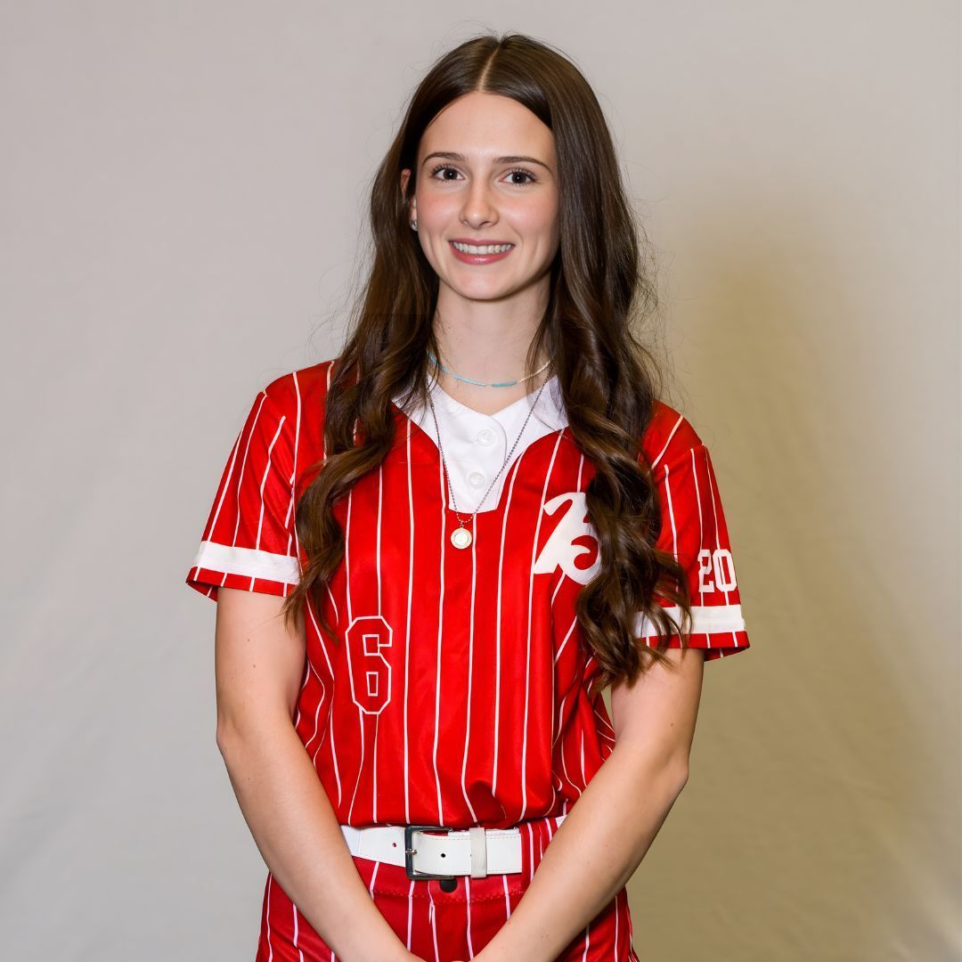 A person smiling in a red and white pinstriped softball uniform, with the number 6 on the front and a white belt.