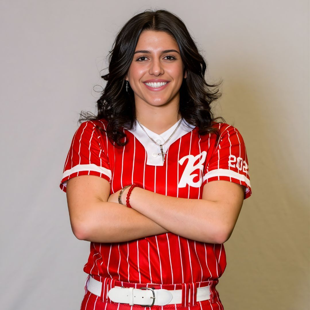 A smiling person in a red, white-striped baseball jersey with arms crossed, set against a plain grey background.