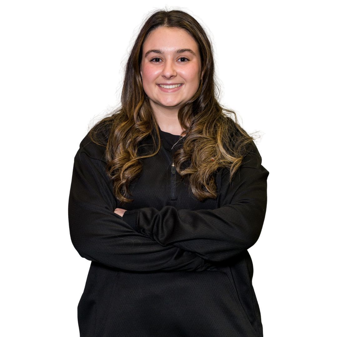 A smiling person with long, wavy brown hair, wearing a black quarter-zip sweatshirt with their arms crossed.