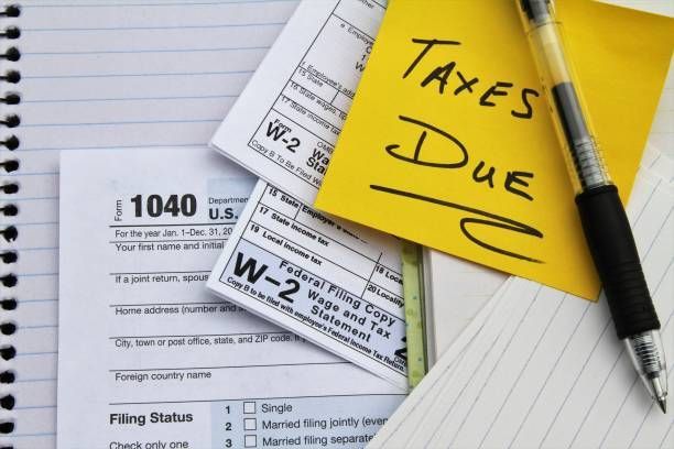 Tax forms, including a 1040 and W-2s, with a Taxes Due sticky note and pen.