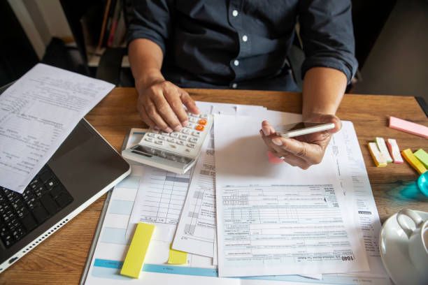 Person calculating taxes at a desk, with calculator, paperwork, laptop, and coffee cup.