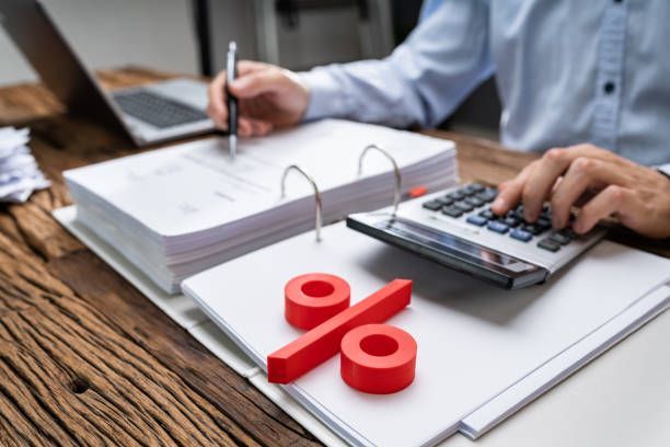 Person calculating with a calculator, working on paperwork, and a red percentage symbol.