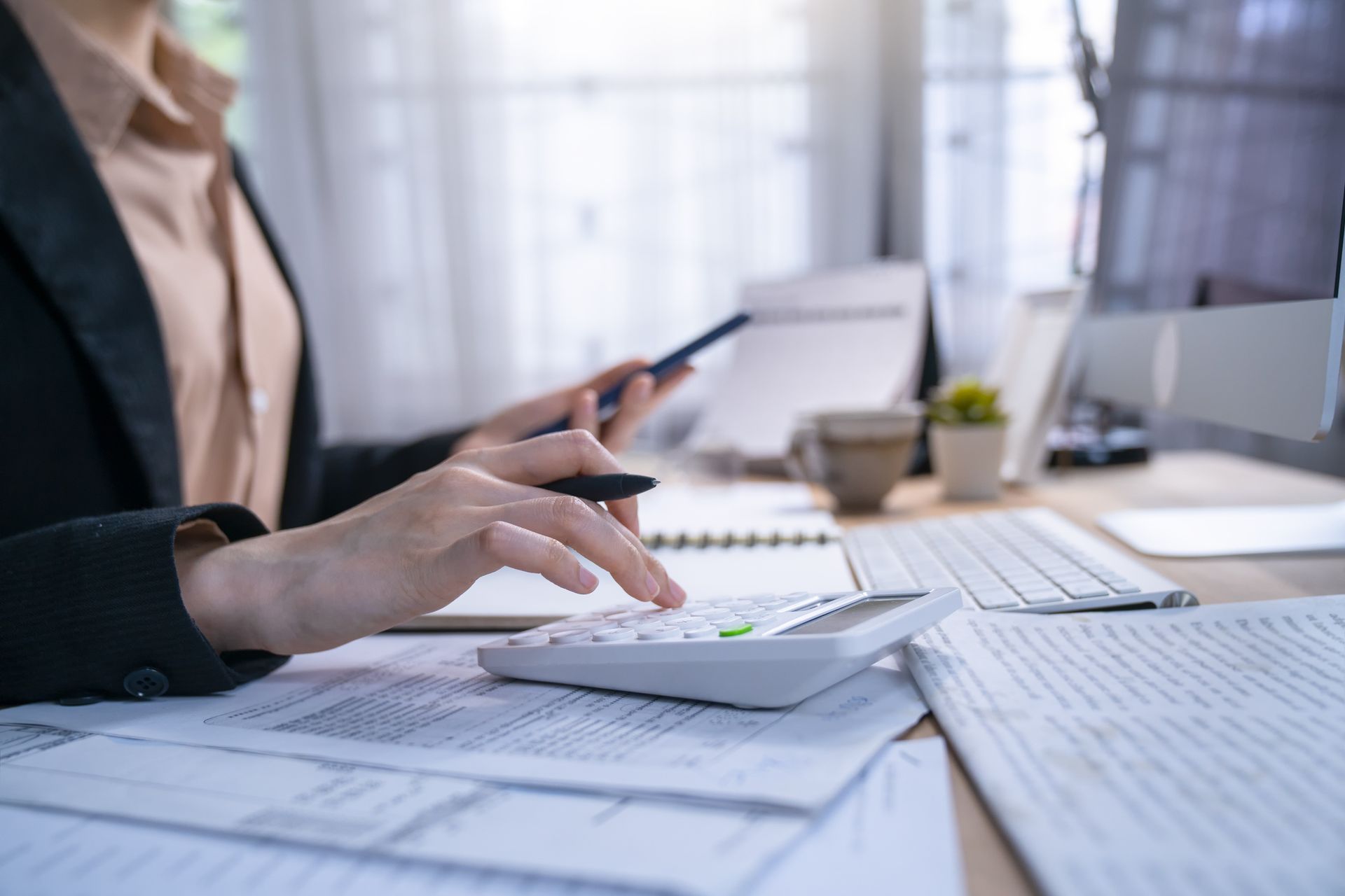 Person calculating with a calculator, documents, phone, and computer on a desk. Person calculating with a calculator, documents, phone, and computer on a desk.