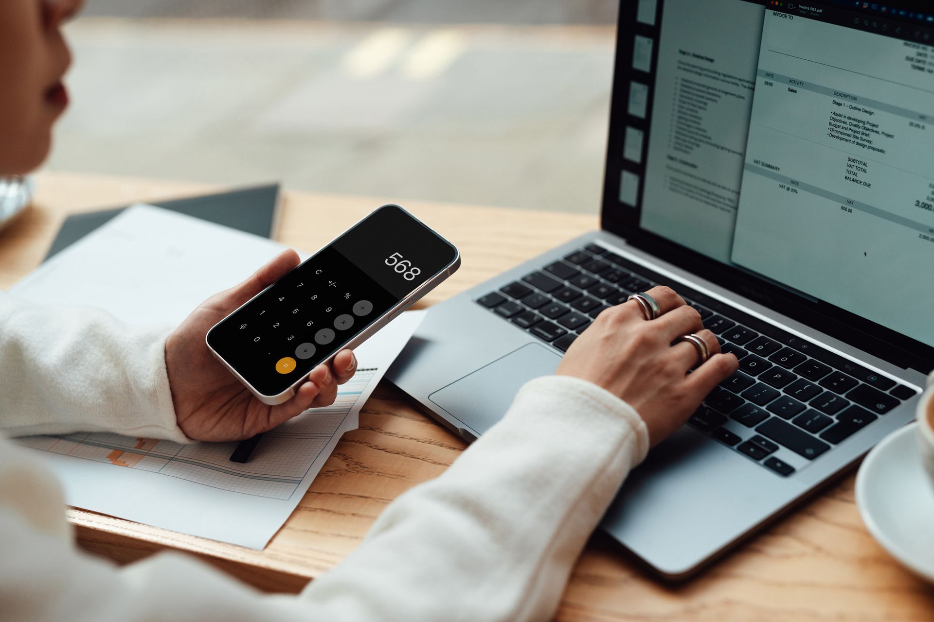 Businesswoman calculating budget with smartphone while making financial plan via laptop.