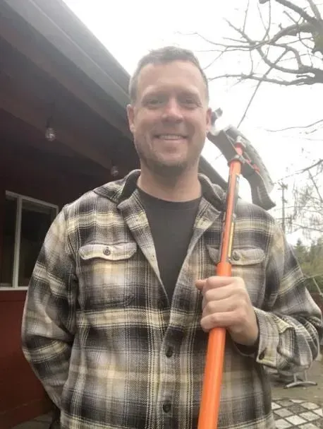 A man in a plaid shirt is holding a hammer and smiling.