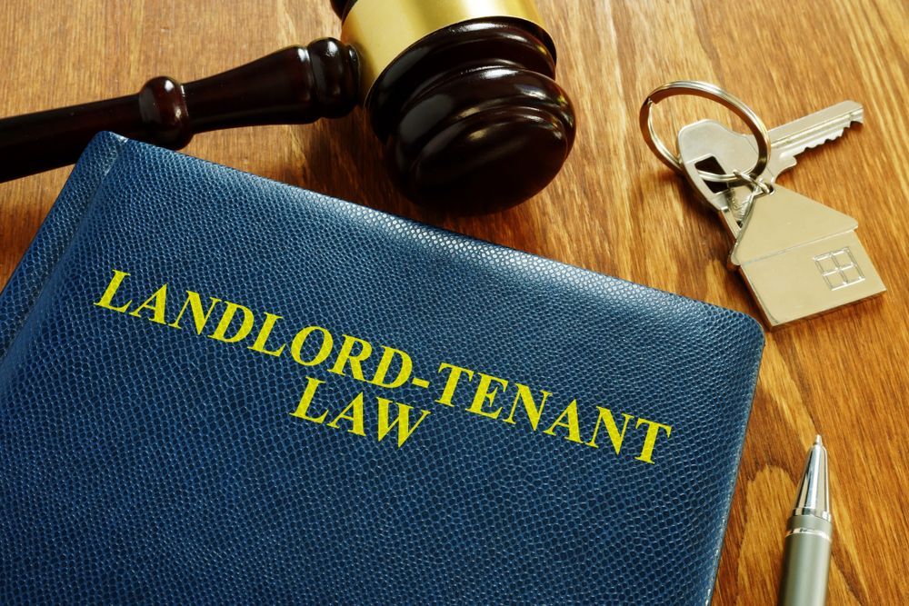 A book titled landlord-tenant law is on a wooden table next to a gavel and keys.