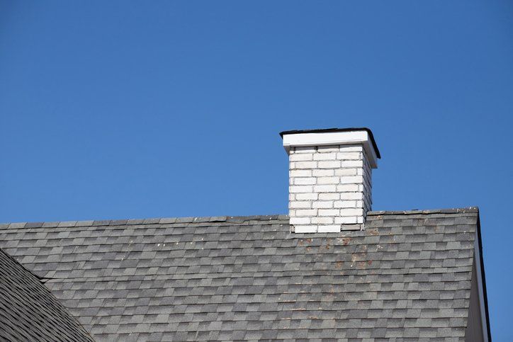 White brick chimney with dirty roof shingle and blue sky