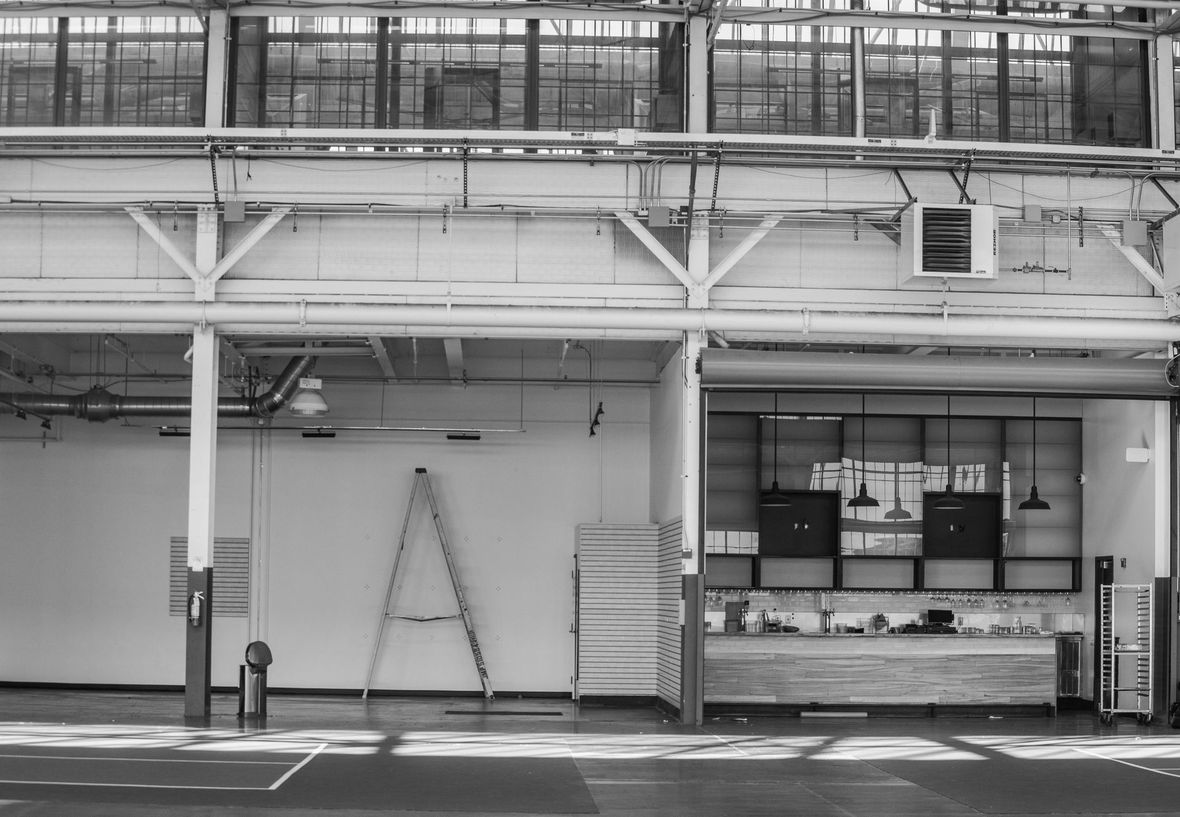 Interior of a large industrial building, with white walls, ladder, and overhead windows.