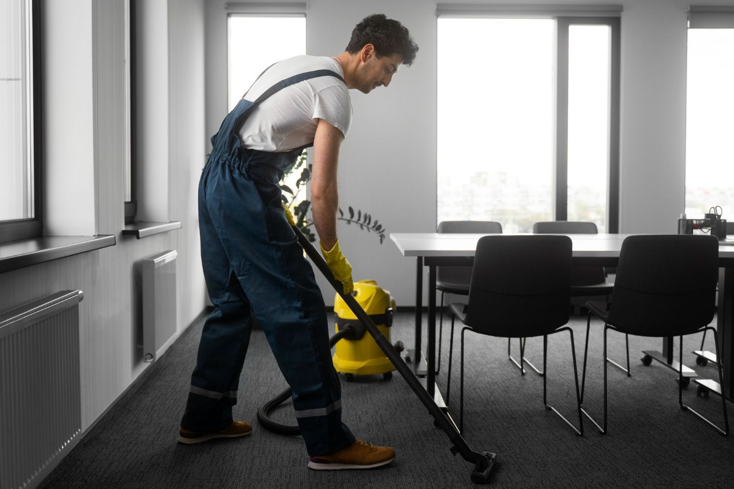 A man is cleaning the floor of an office with a vacuum cleaner.