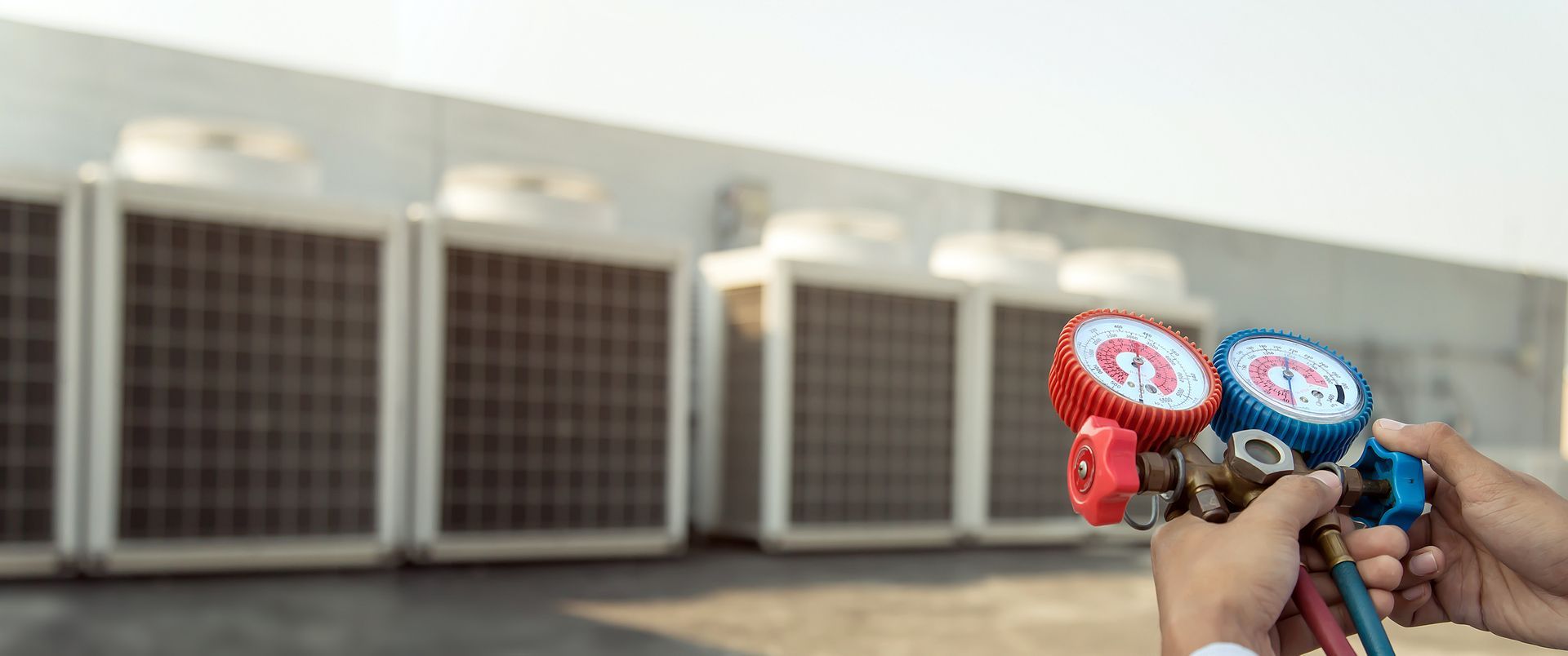 Hands holding gauges in front of air conditioning units on a rooftop.