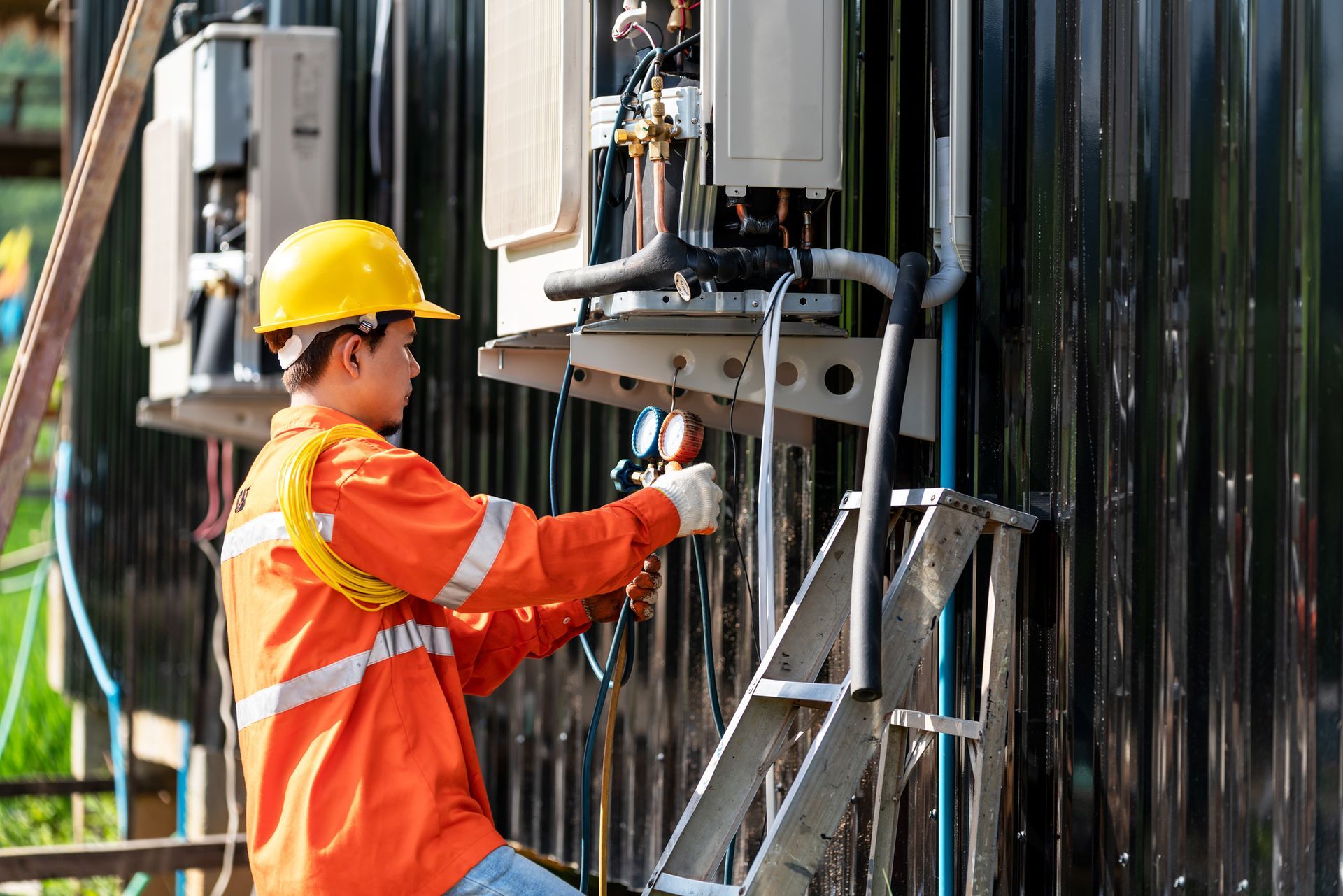 Worker in safety gear repairs outdoor electrical equipment.