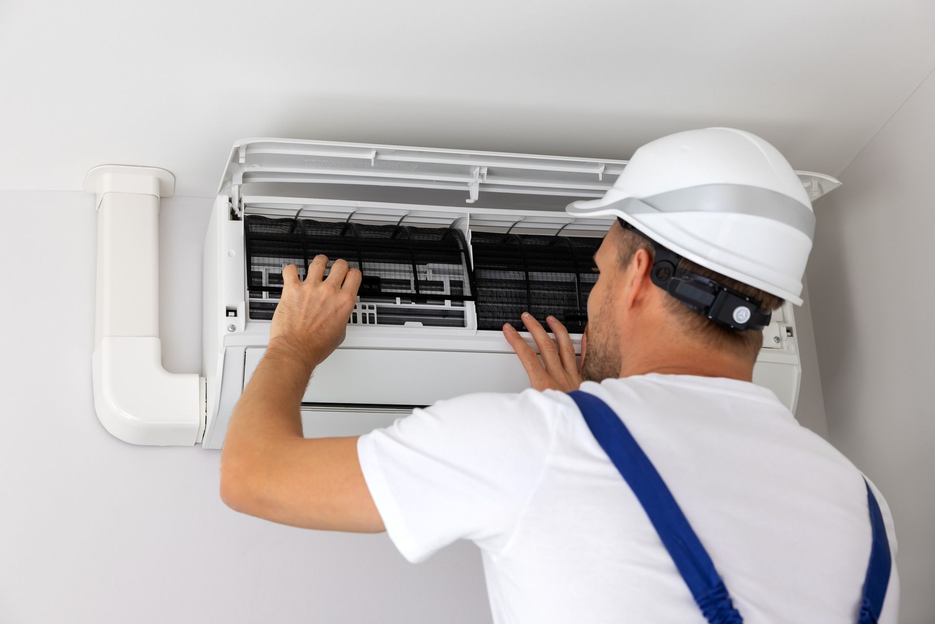 HVAC technician in white hardhat and overalls cleaning an air conditioner filter.
