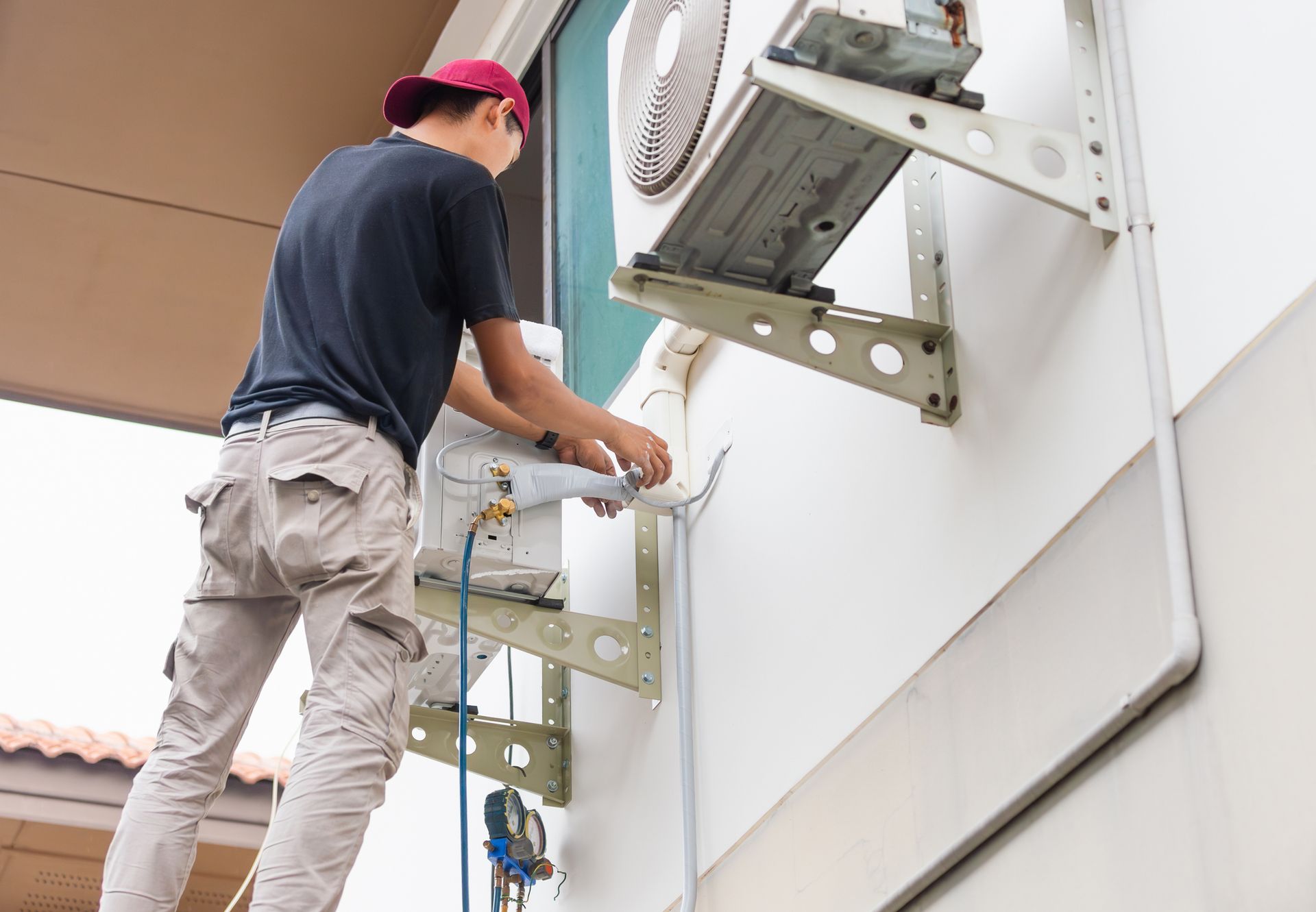 Person on ladder, servicing an outdoor air conditioning unit mounted on a wall.