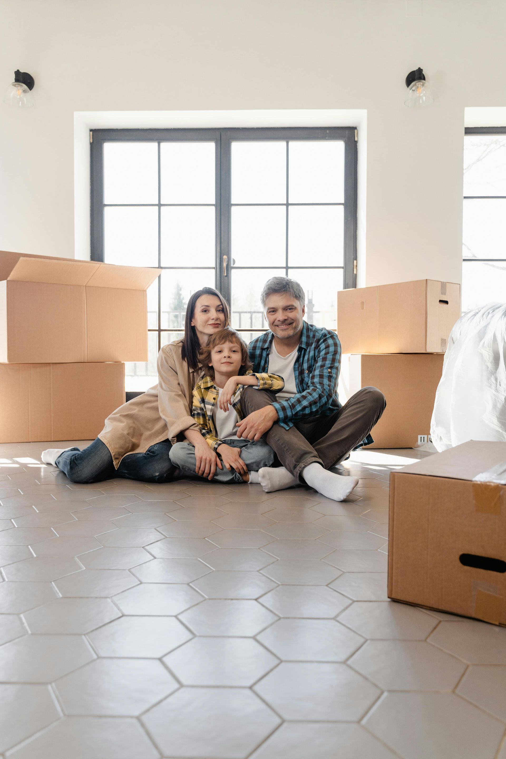 A family is sitting on the floor in their new home surrounded by cardboard boxes.