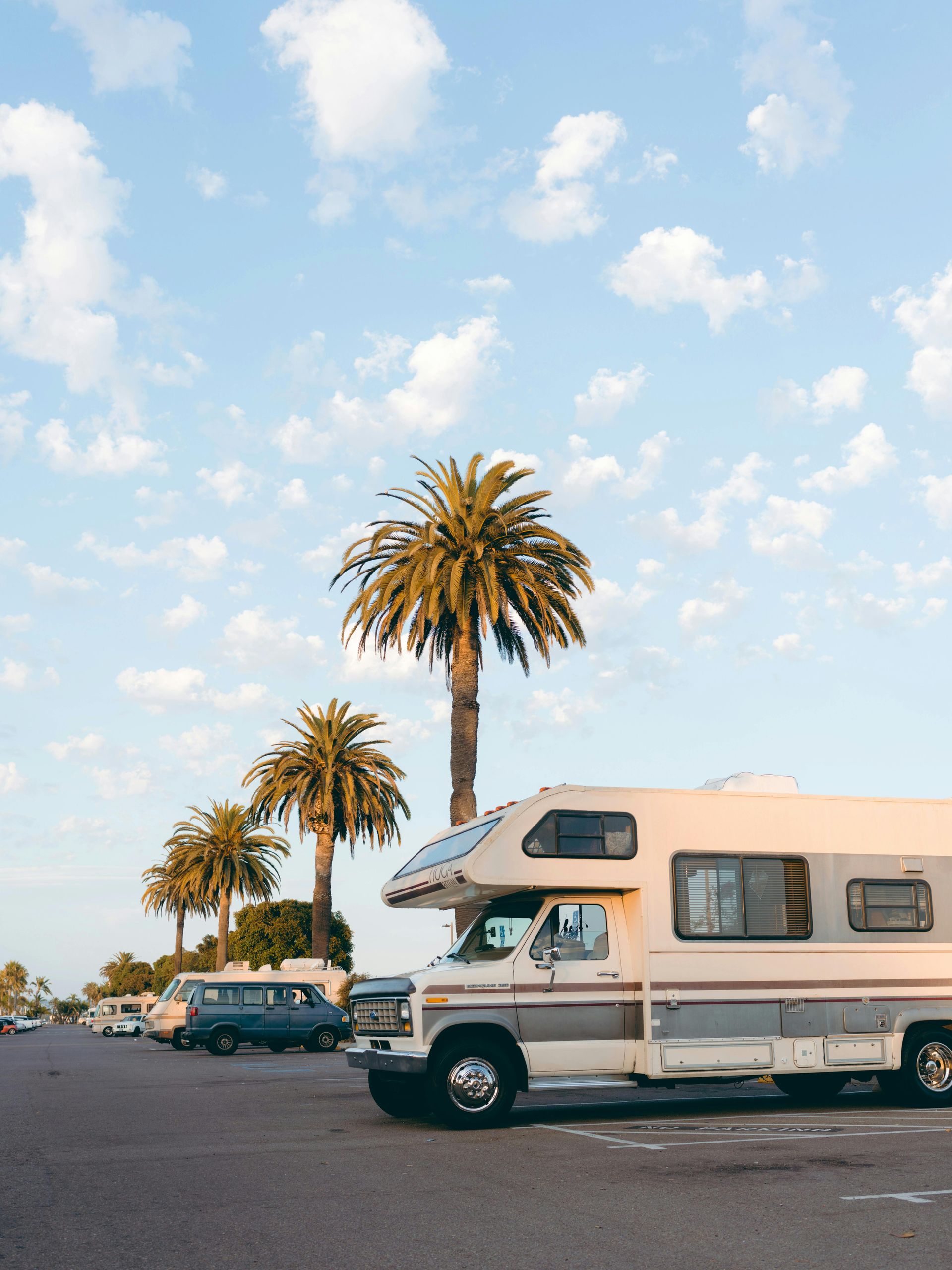 A rv is parked in a parking lot with palm trees in the background.