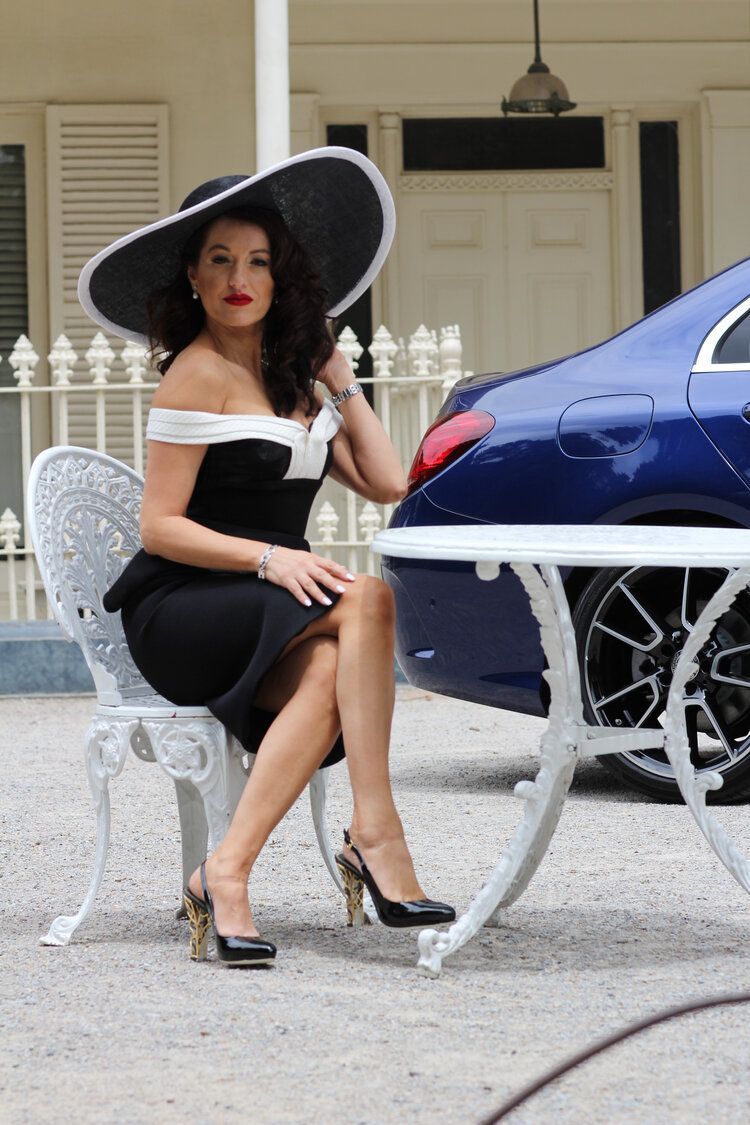 A woman in a black and white dress is sitting at a table in front of a blue car.