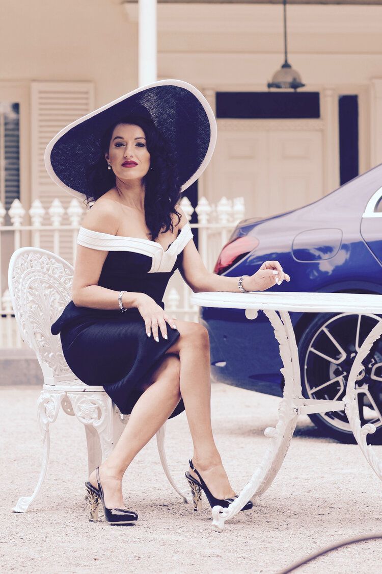 A woman in a hat is sitting at a table in front of a blue car.