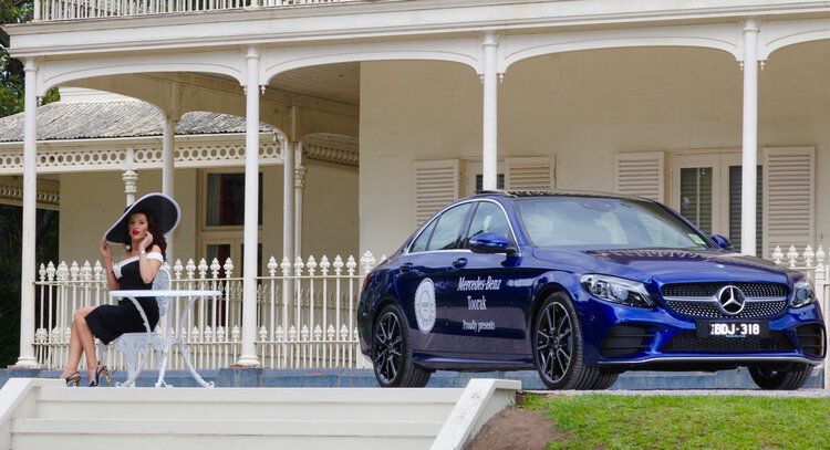 A woman is sitting at a table in front of a blue mercedes benz.