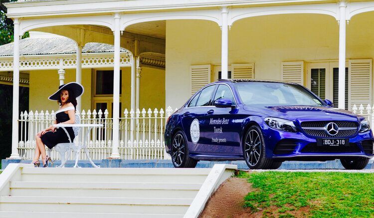 A woman is sitting at a table in front of a blue car.