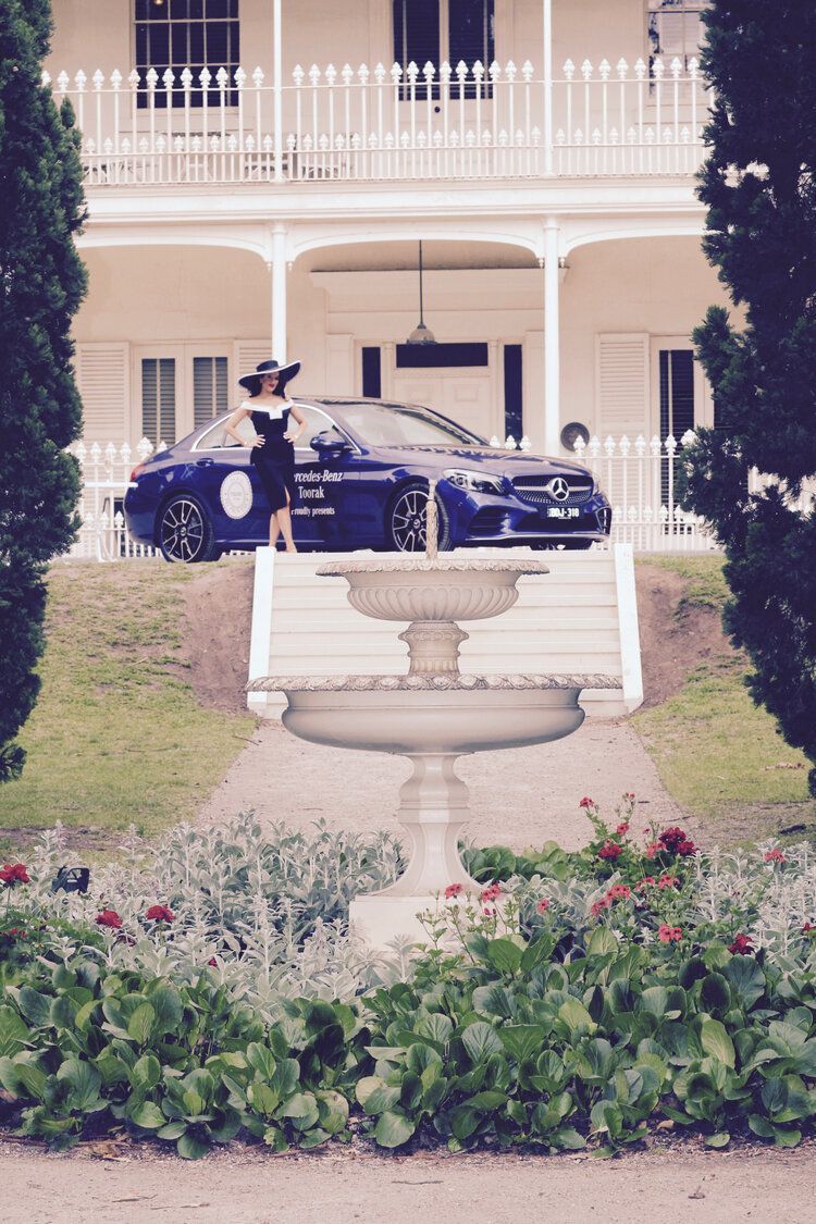 A woman in a black dress is standing in front of a blue car.