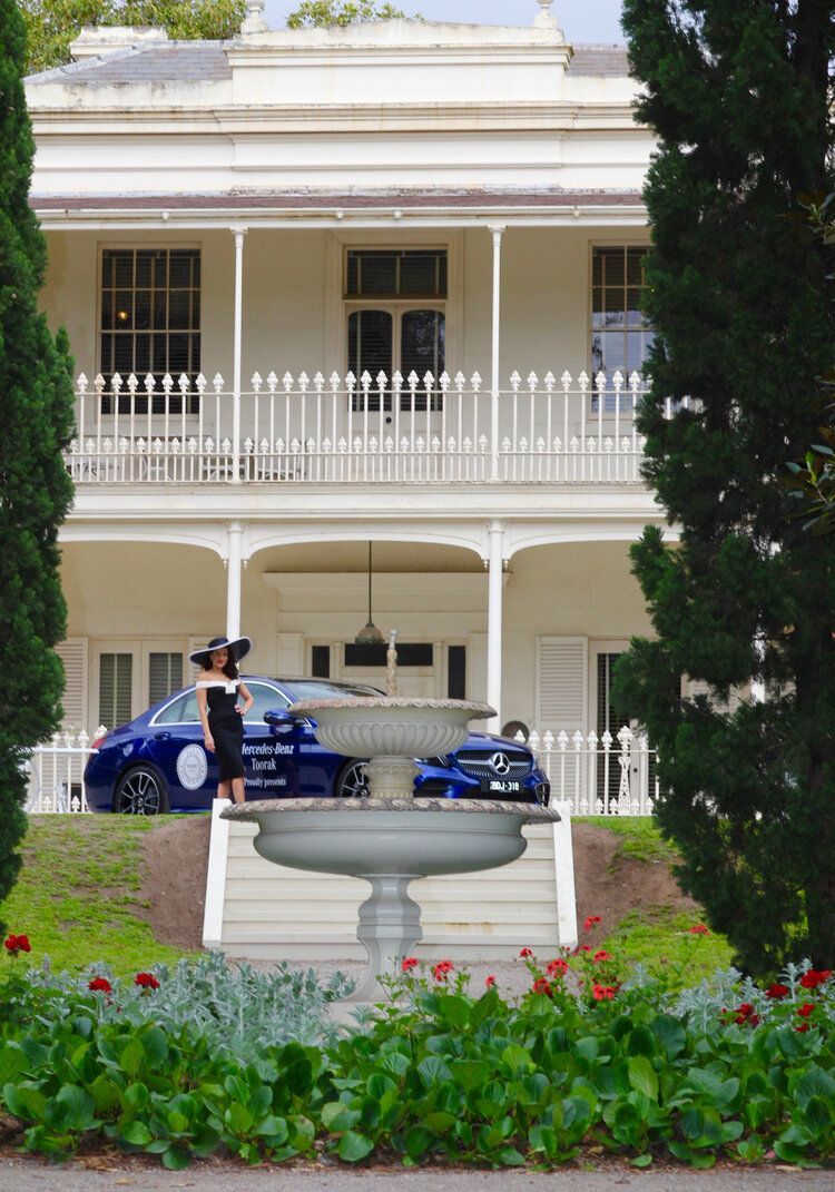 A woman in a black dress is standing in front of a large white house.