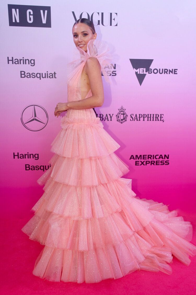 A woman in a pink dress is standing on a pink carpet.