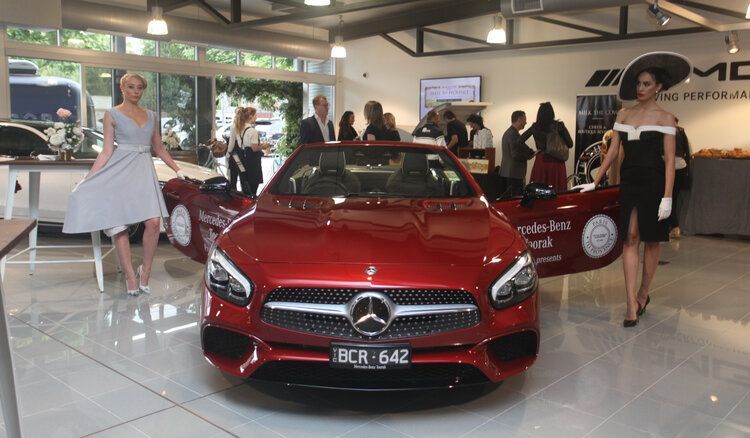 Two women are standing in front of a red mercedes car.