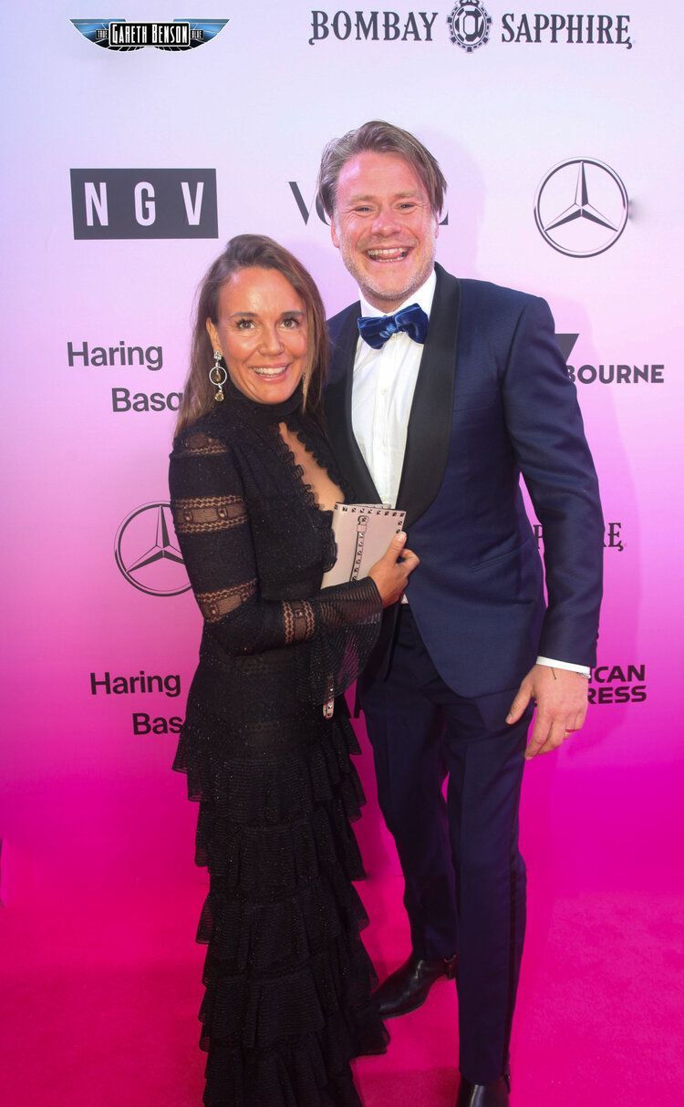 A man and a woman are posing for a picture on a pink carpet.
