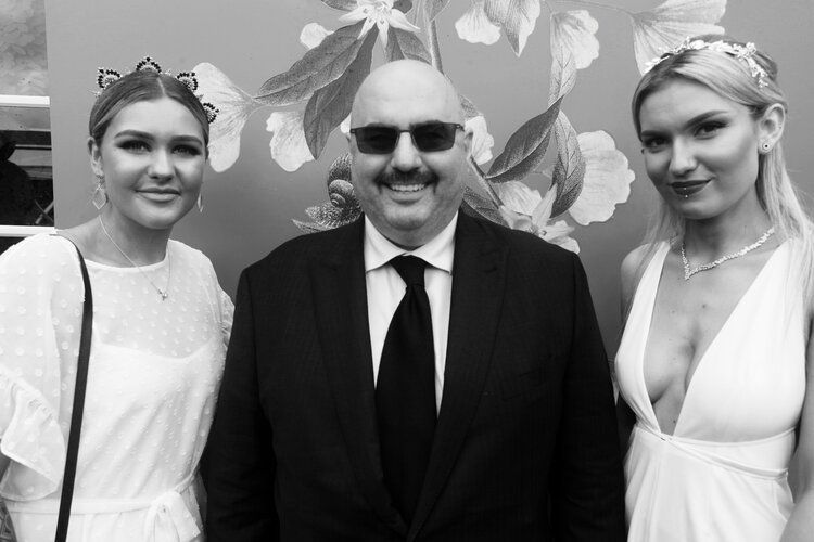 A man in a suit and tie is standing next to two women in white dresses.