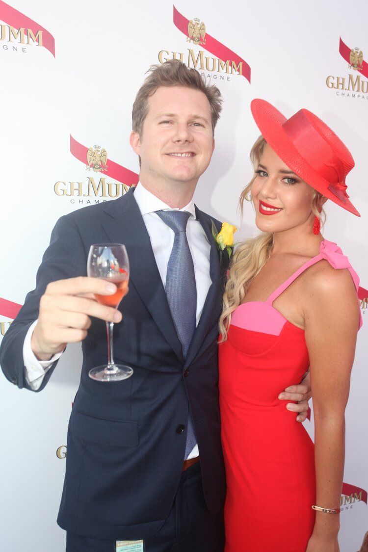 A man in a suit and tie holds a glass of wine next to a woman in a red dress