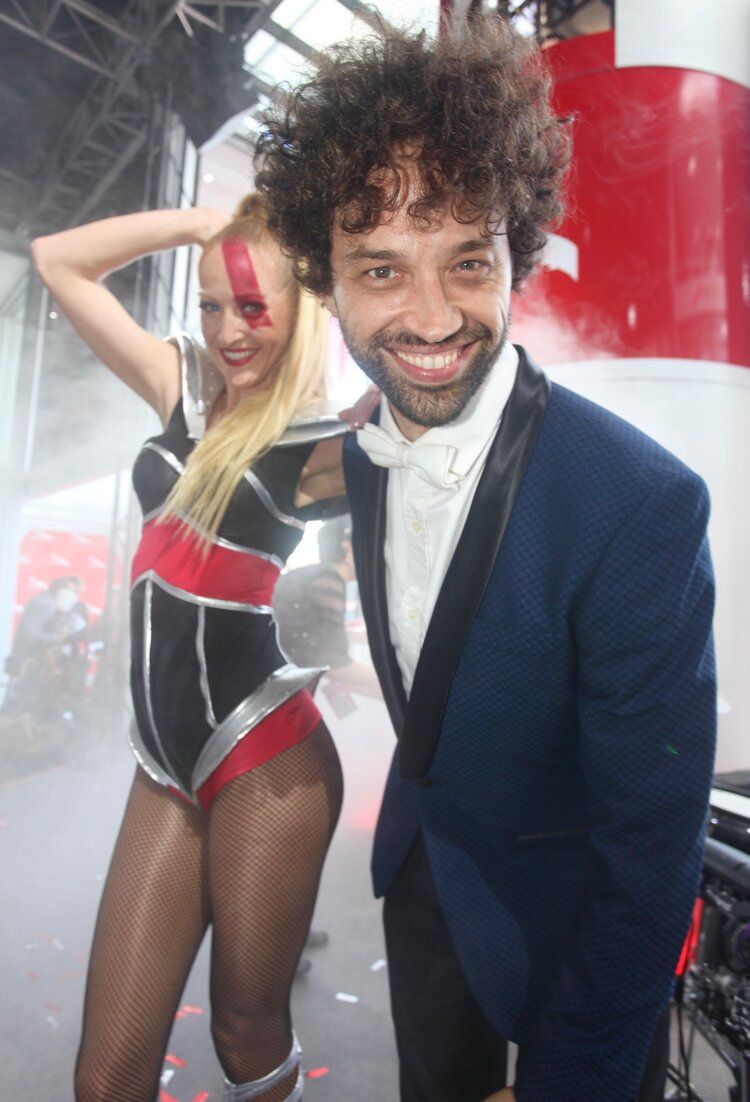 A man in a suit is standing next to a woman in a bodysuit.