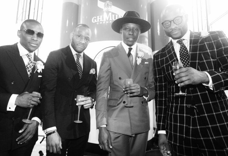 A black and white photo of four men in suits holding champagne glasses