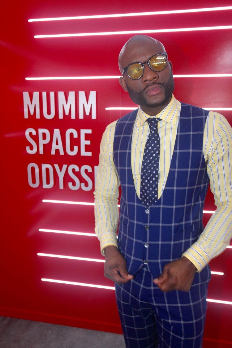 A man in a suit and tie is standing in front of a sign that says mumm space odyssey