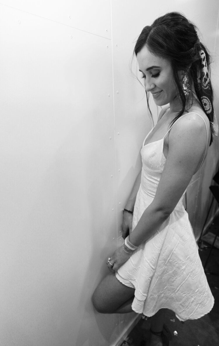 A woman in a white dress is kneeling down in front of a wall.