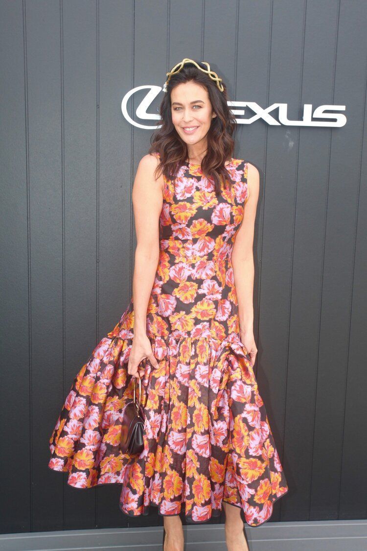A woman in a floral dress is standing in front of a lexus sign.