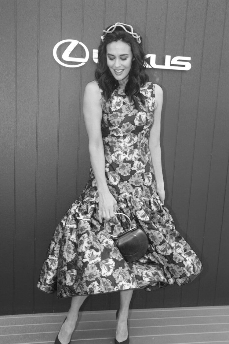 A woman in a floral dress is standing in front of a lexus sign.