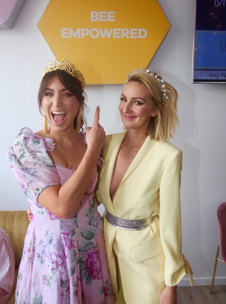 Two women are posing for a picture in front of a sign that says bee empowered