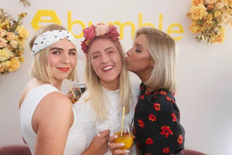 Three women are posing for a picture and one of them is kissing another woman on the cheek.
