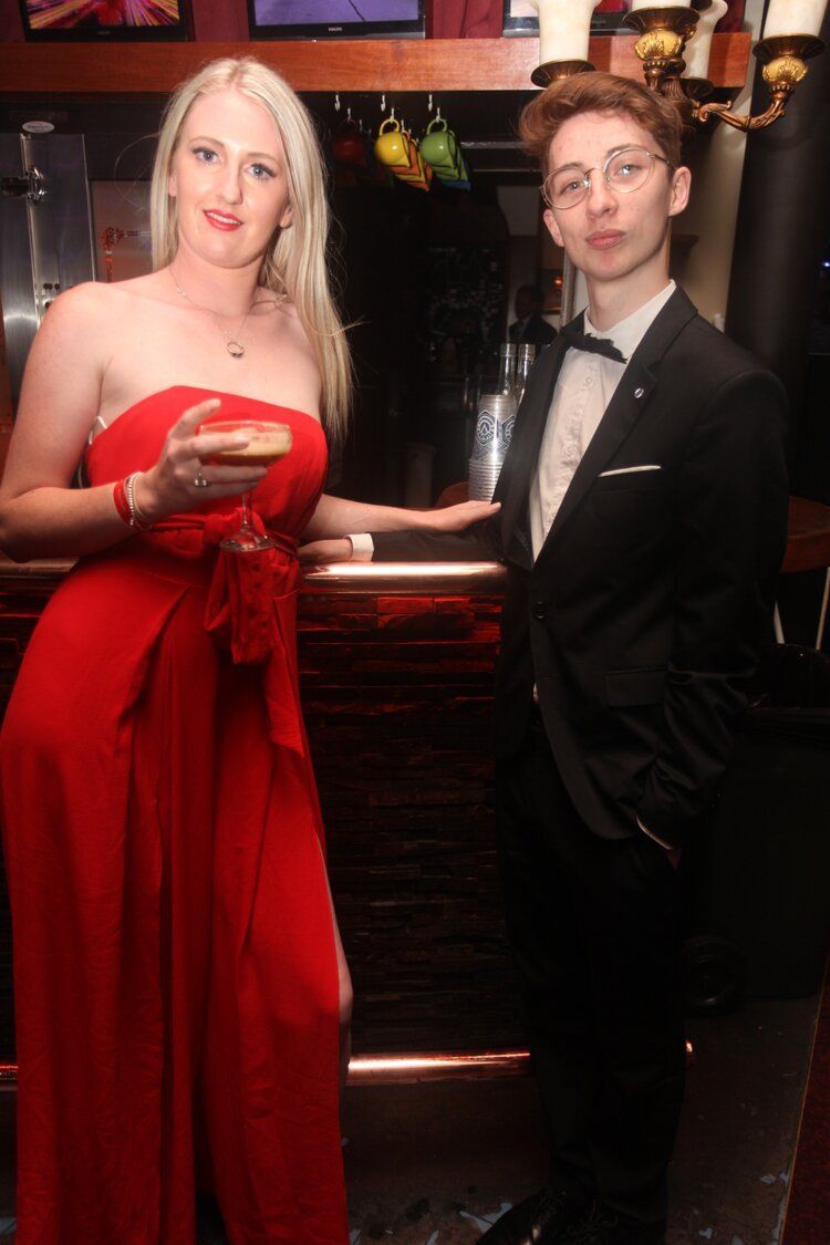 A woman in a red dress is standing next to a man in a tuxedo.