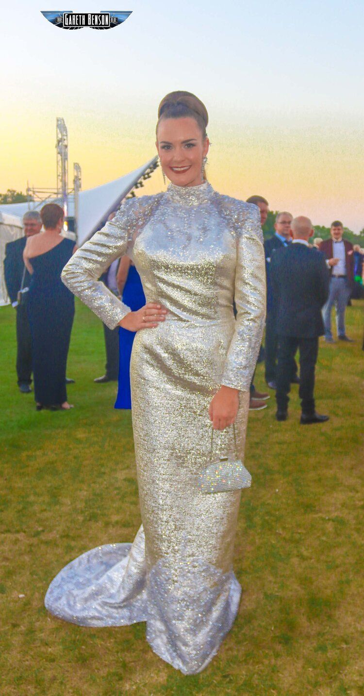 A woman in a long silver dress is standing in the grass.