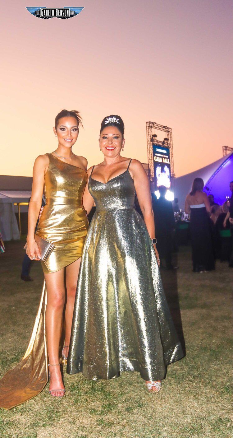 Two women in gold dresses are standing next to each other in a field.