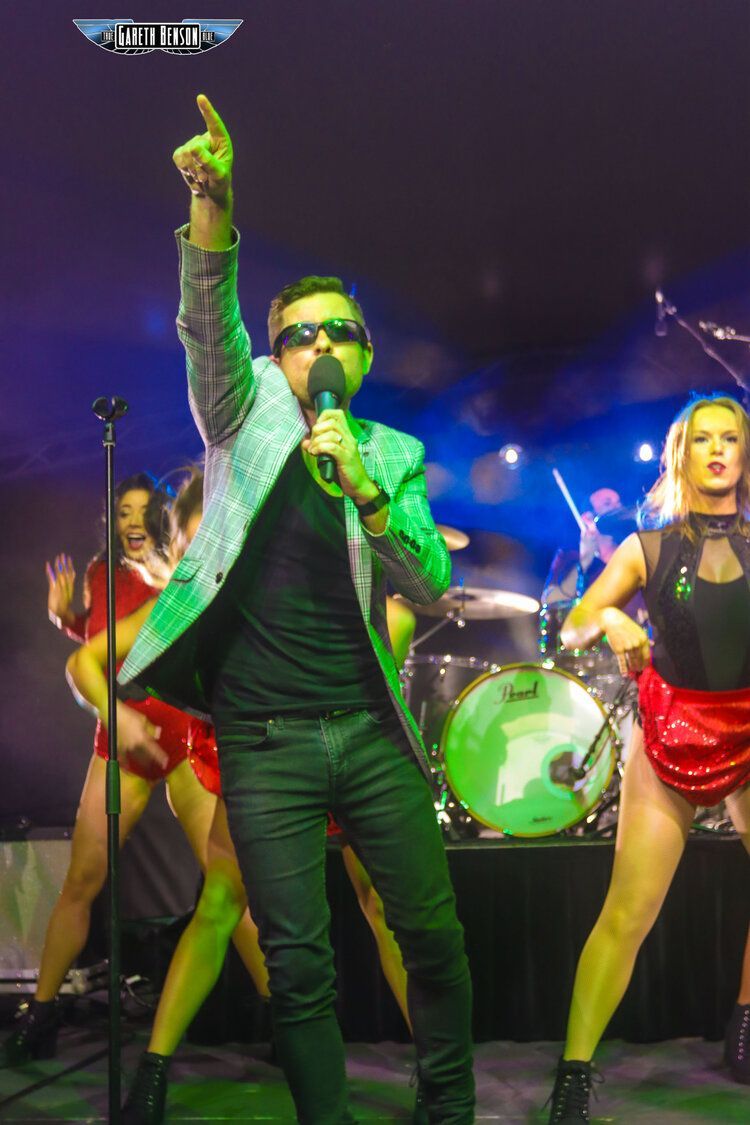 A man in a green jacket is singing into a microphone on a stage.