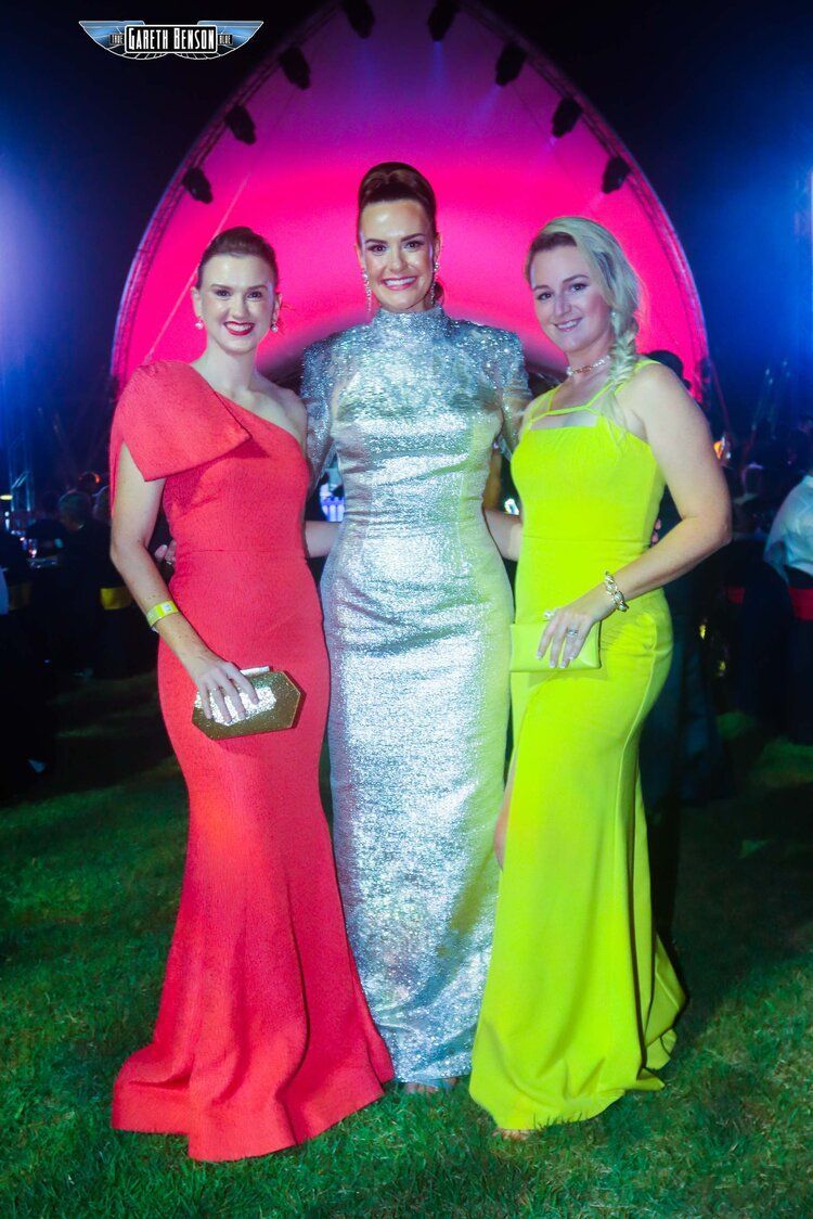 Three women in long dresses are posing for a picture.